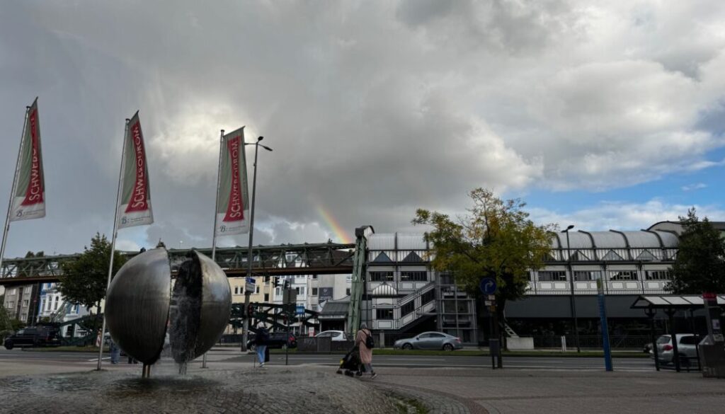 Kugelbrunnen, Schwebodromfahnen, im Hintergrund ein Regenbogen über der Schwebebahnhaltestelle Werther Brücke