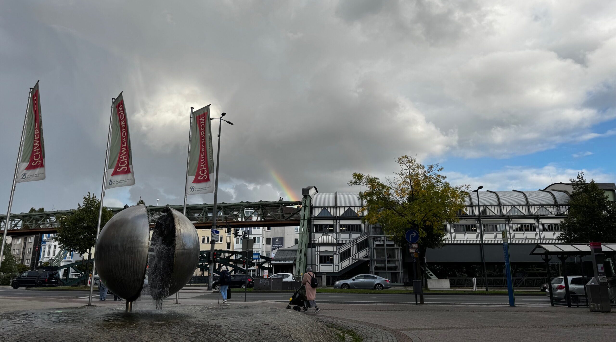 Kugelbrunnen, Schwebodromfahnen, im Hintergrund ein Regenbogen über der Schwebebahnhaltestelle Werther Brücke