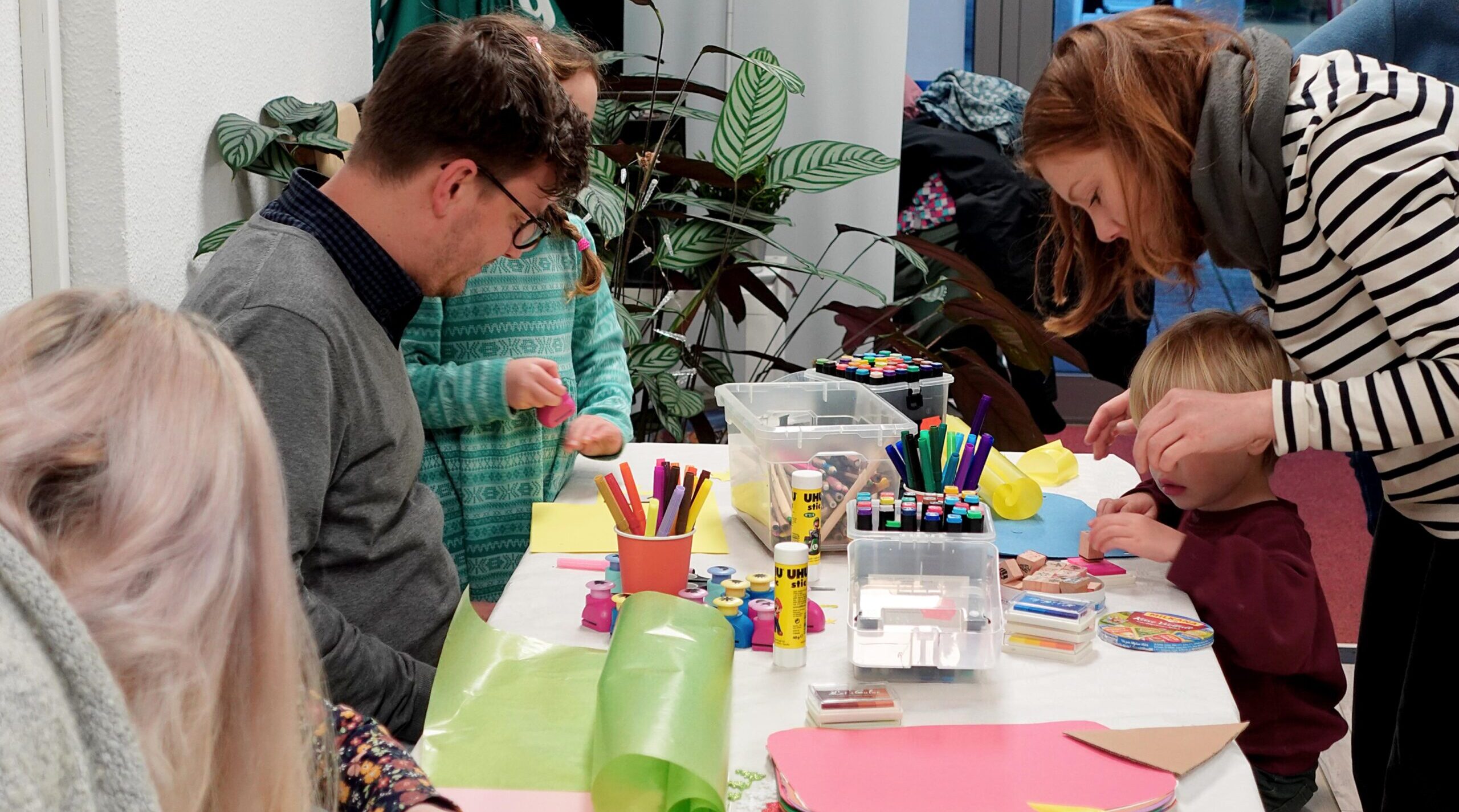 Erwachsene und Kinder sitzen am Tisch der mit Bastelmaterial bedeckt ist